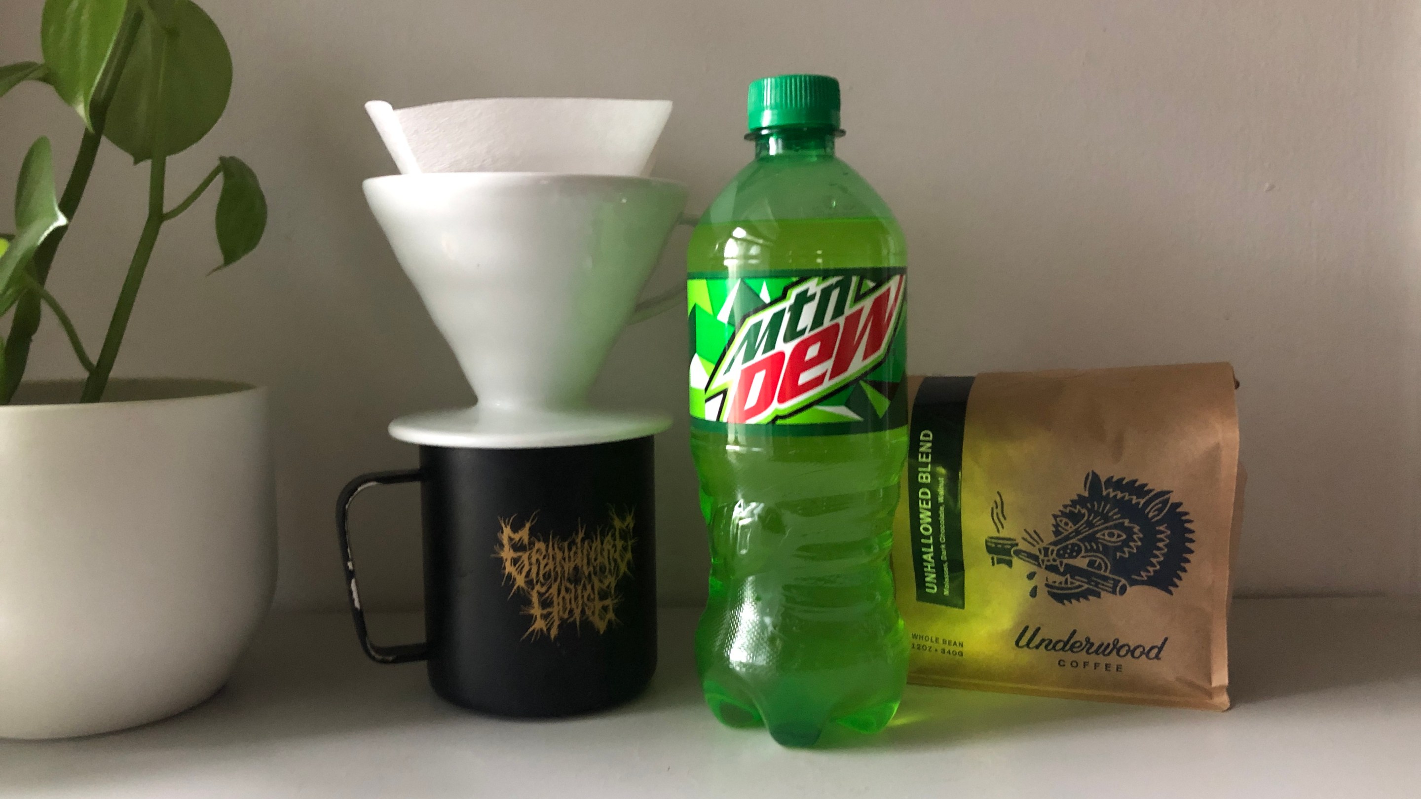 A lime-green bottle of Mountain Dew next to a bag of coffee beans and a pourover and mug.