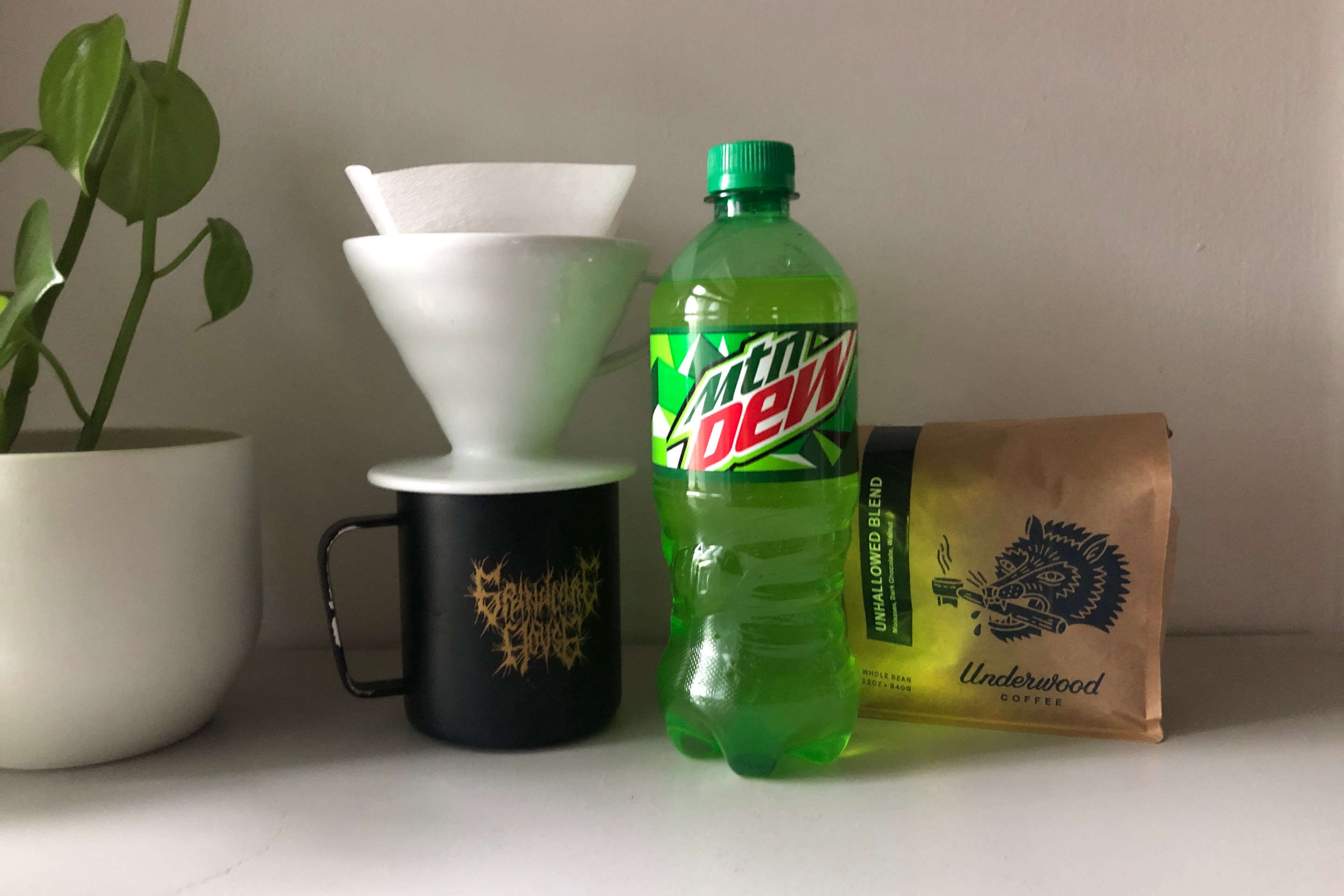 A lime-green bottle of Mountain Dew next to a bag of coffee beans and a pourover and mug.