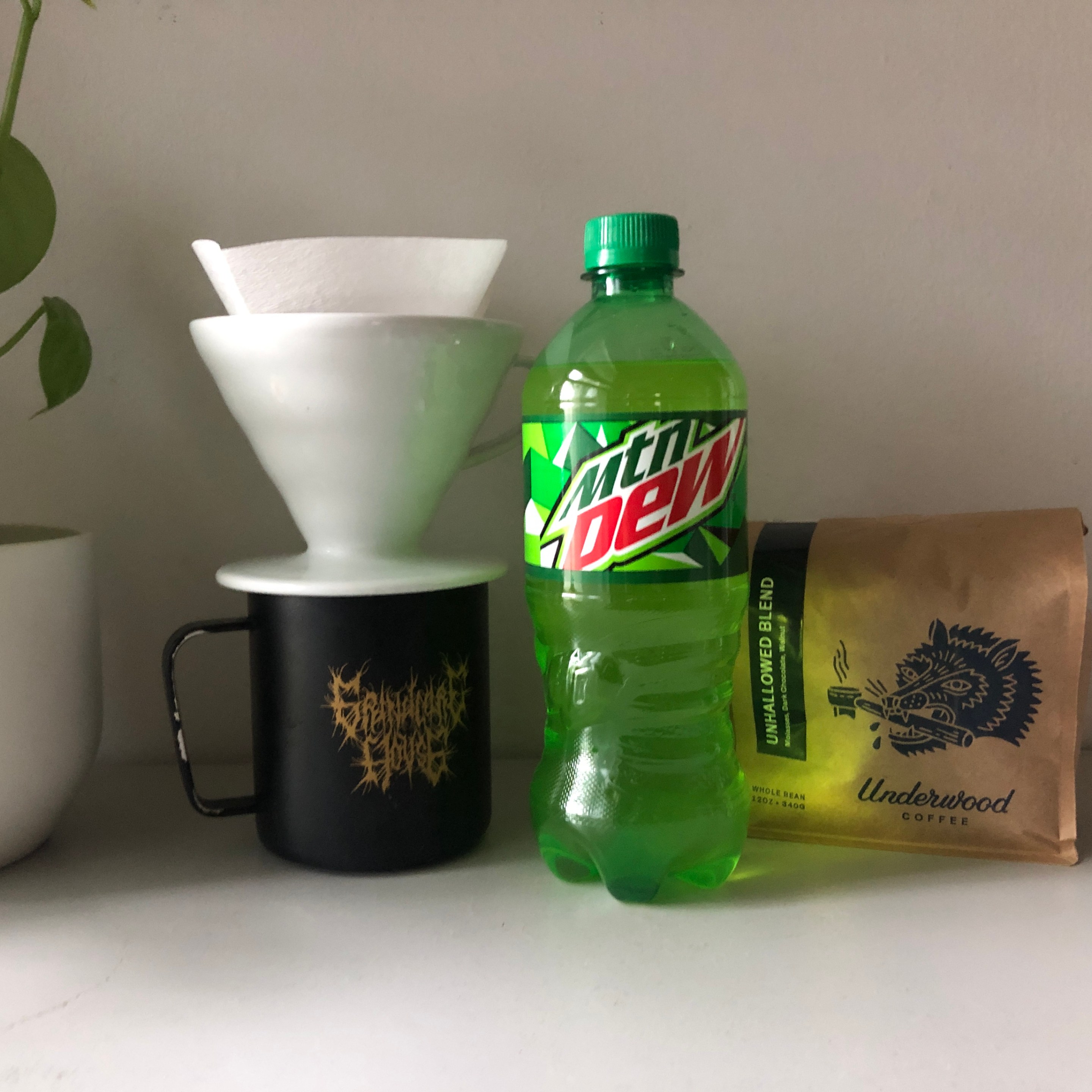 A lime-green bottle of Mountain Dew next to a bag of coffee beans and a pourover and mug.