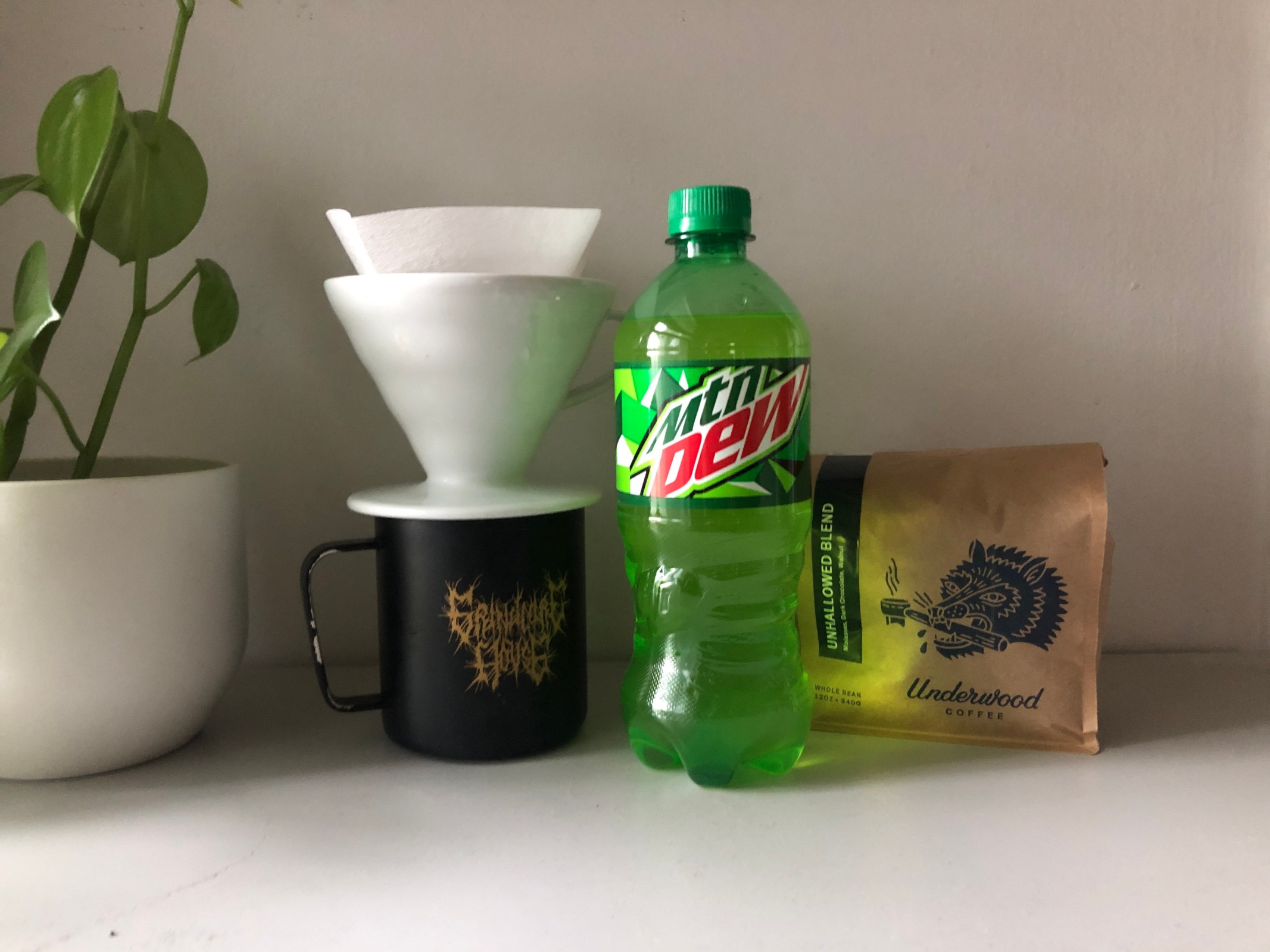 A lime-green bottle of Mountain Dew next to a bag of coffee beans and a pourover and mug.
