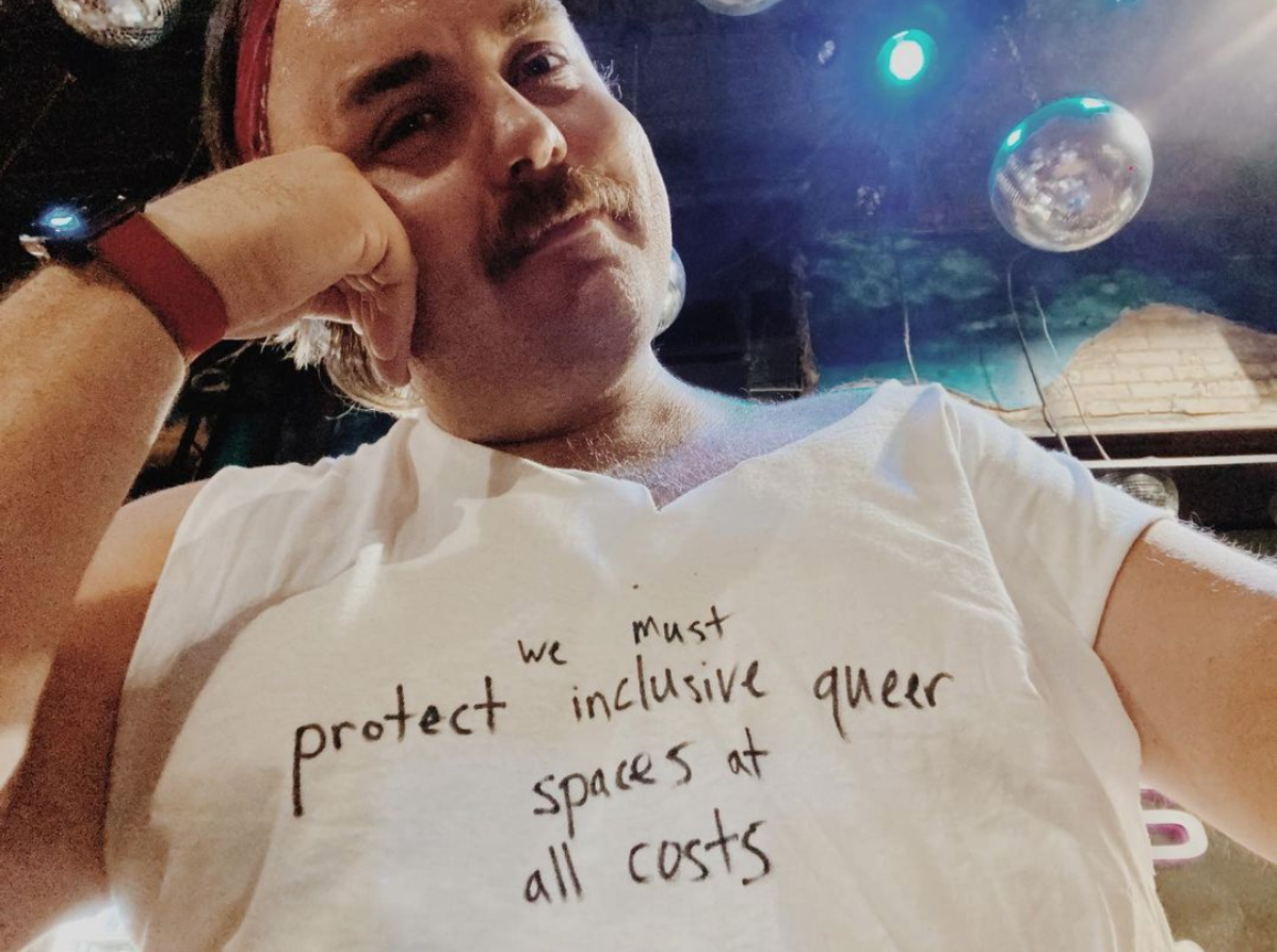 Spencer Retelle in a T shirt reading "w must protect inclusive queer spaces at all costs"