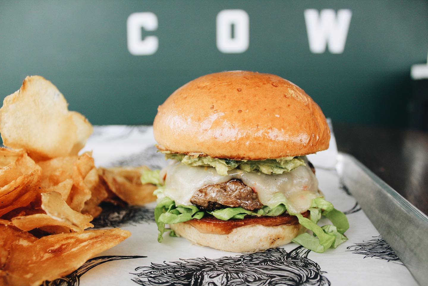 a copper cow burger and chips photographed in front of a wall reading "cow"