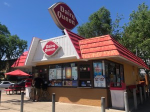 An exterior shot of the Dairy Queen on 38th Street. A person with a bike is ordering at the window.