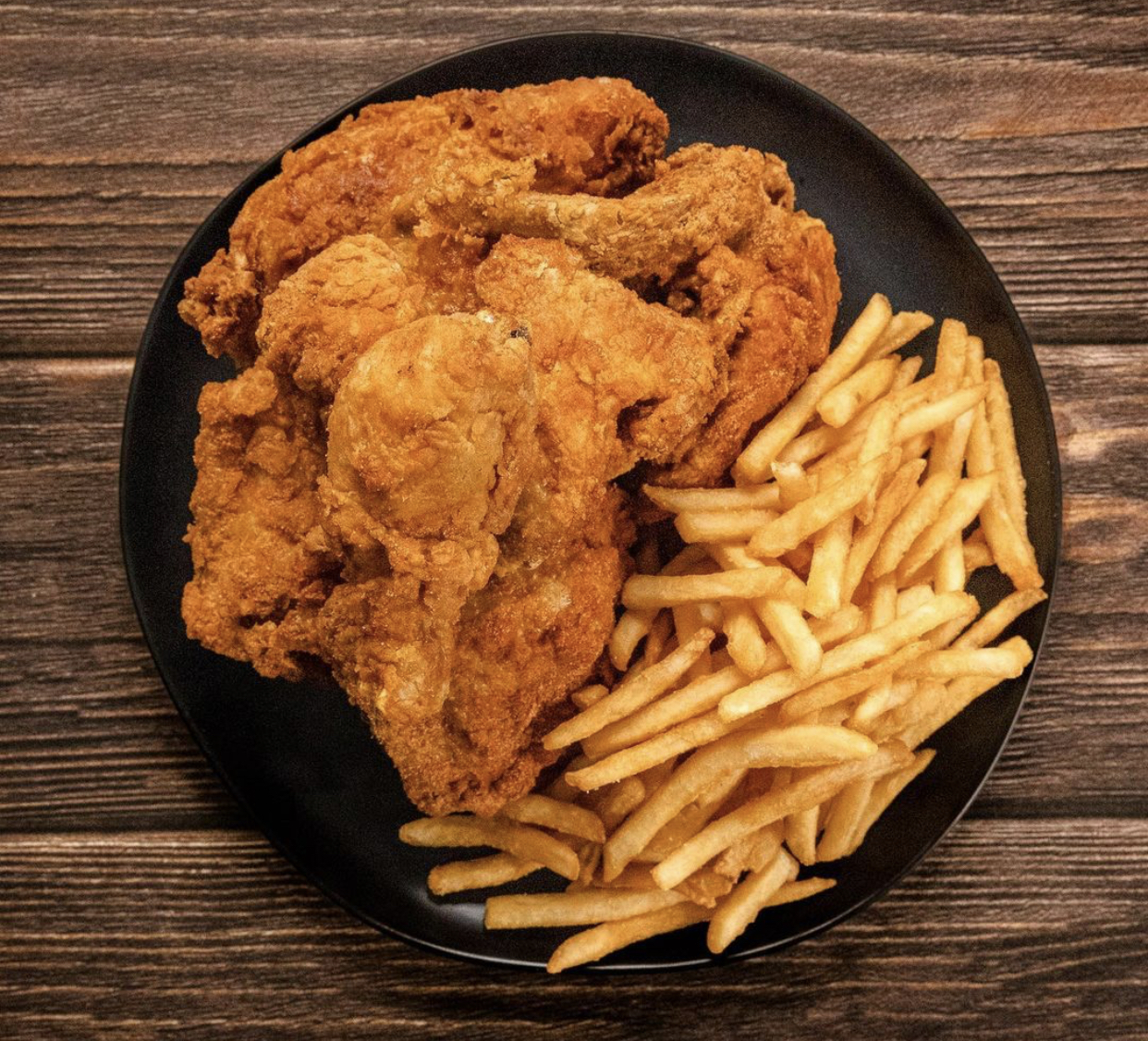 an overhead shot of a platter of fried chicken and french fries on a wooden table