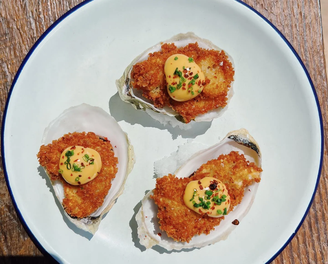 an overhead shot of three fried oysters dotted with bright-yellow smoked fresno aioli
