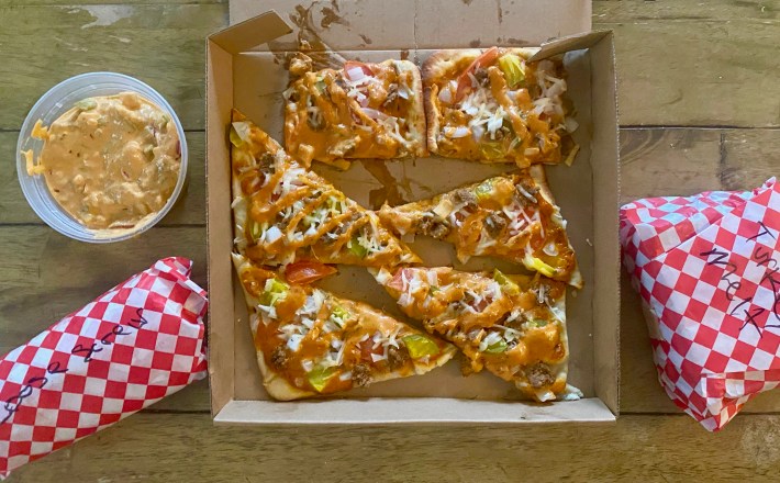 Overhead shot of Insane Vegan's cheeseburger pizza and two sandwiches wrapped in red checkered paper
