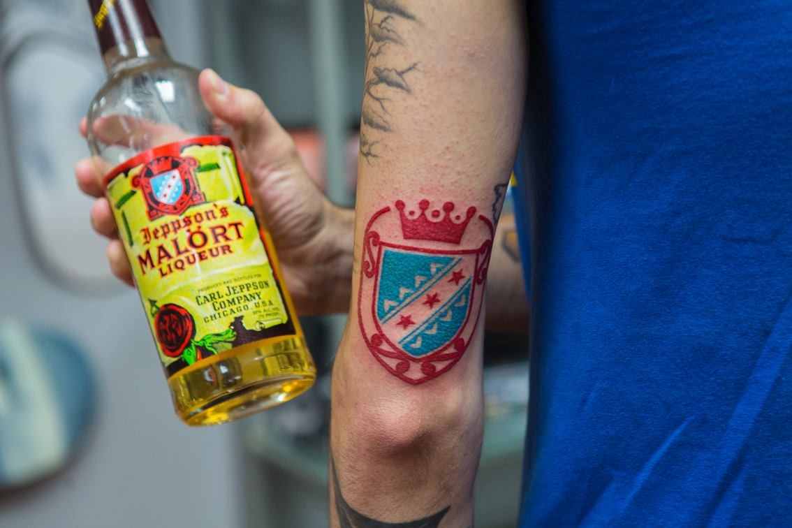 a man holds a bottle of malort while showing off his malort tattoo