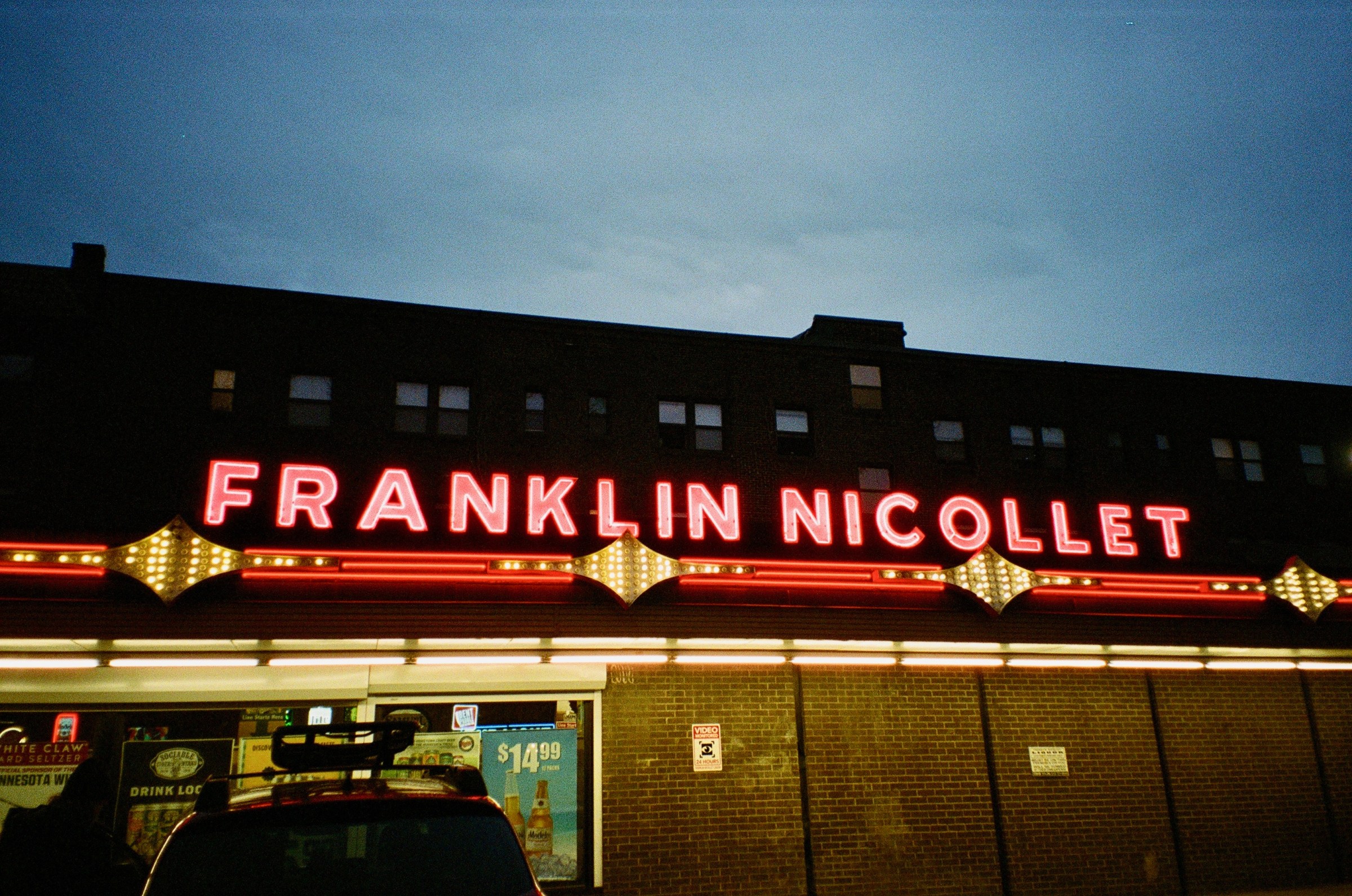 a nighttime shot of the neon sign in front of franklin nicollet liquors