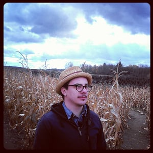 a guy in a hat and jacket stands in a corn maze