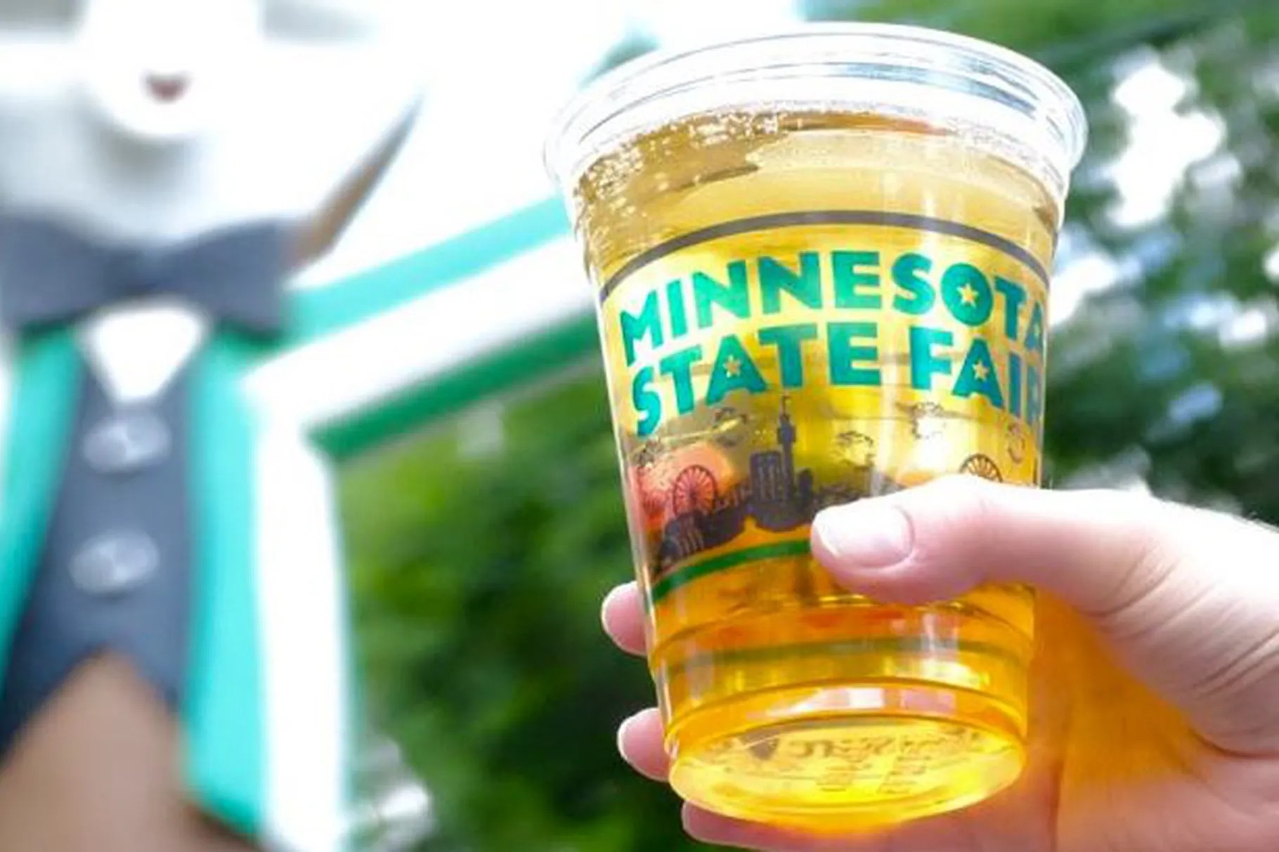a hand triumphantly hoists a beer in an official Minnesota State Fair plastic cup into the air