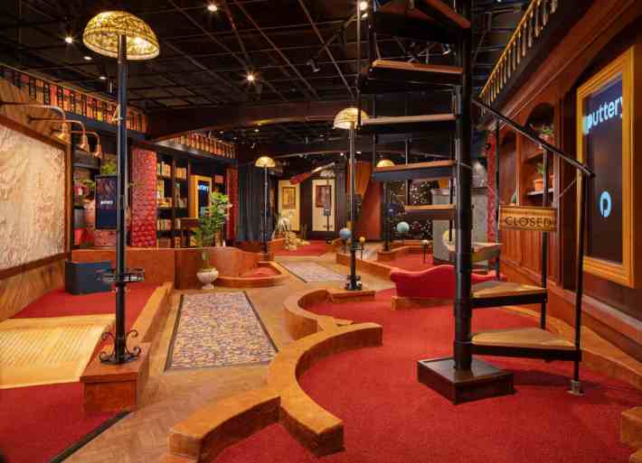 a gaudy red carpeted, high ceilinged room with a winding staircase and several mini golf courses