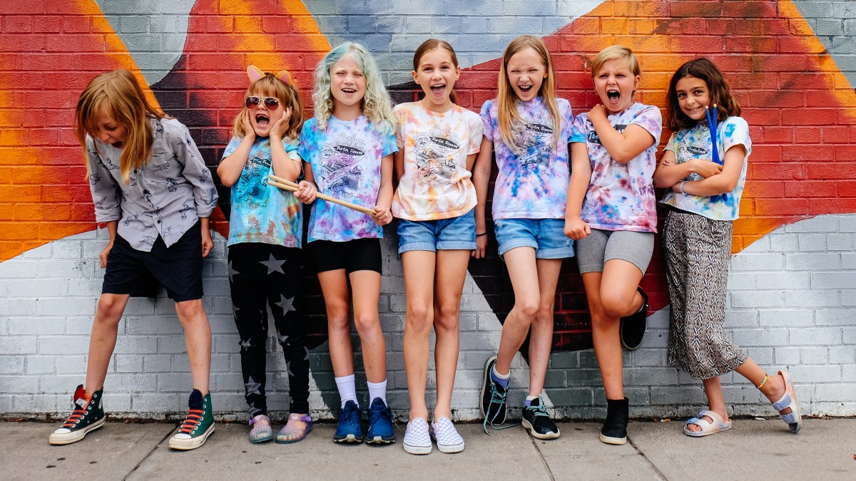 seven young girls in tie dye shirts pose screaming in front of a wall