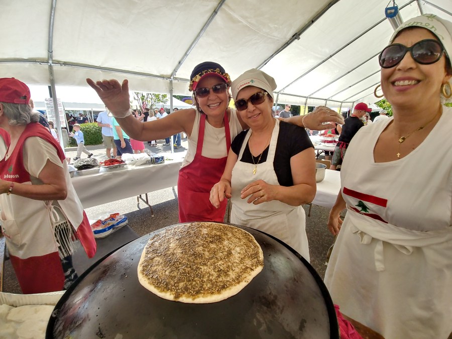 four people smile and prepare food on a wide griddle