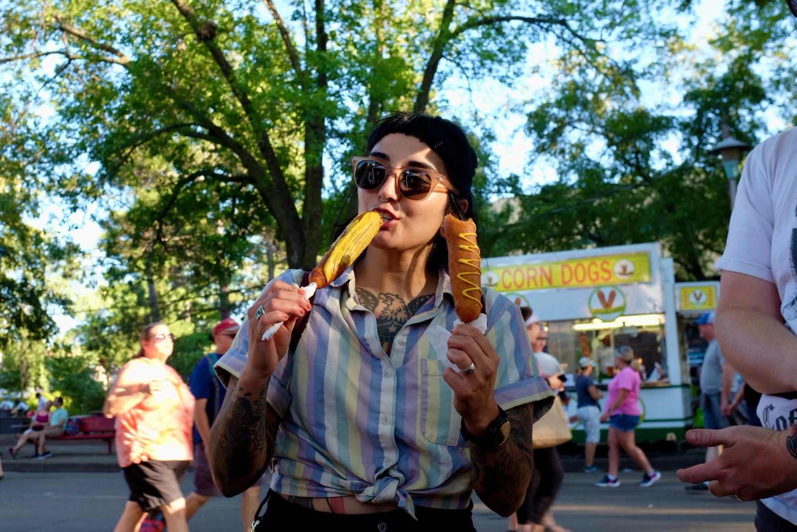 A hot dog expert holds two tube meats on sticks, one covered in mustard, and one with a thin drizzle of it