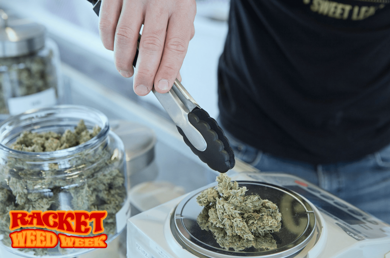 a hand holding tongs over a scale loaded up with cannabis flower