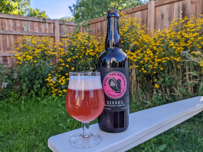 a rosy red beer in a glass in a yard full of yellow wildflowers