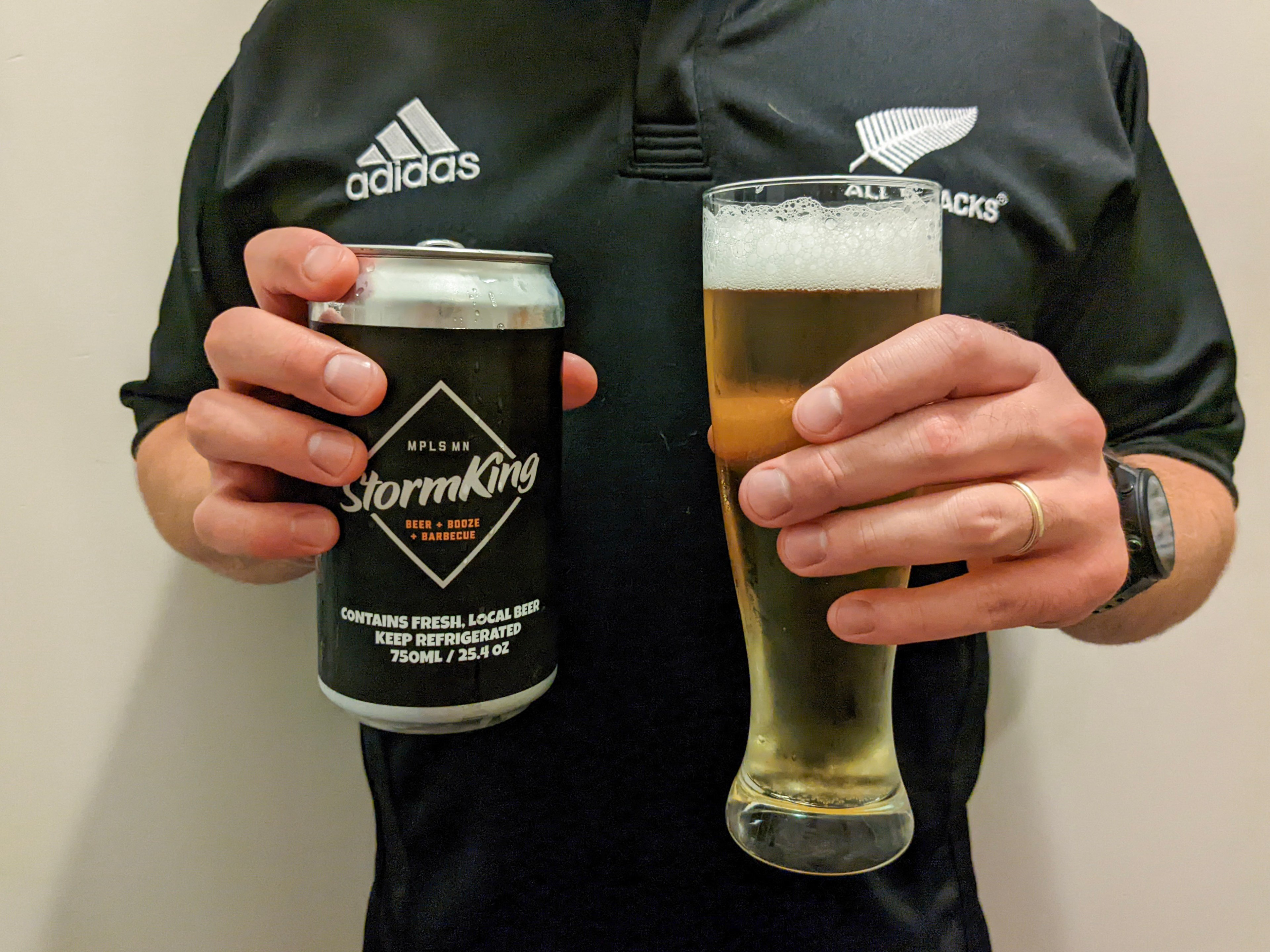 a pair of hands holding the black beer can and a glass