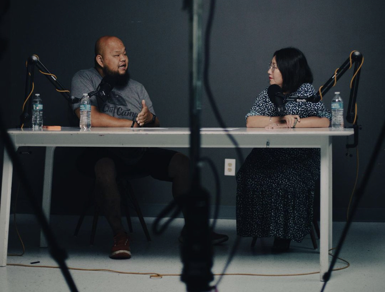 Yia Vang and Kao Kalia Yang sit at a table recording an episode of the Hmonglish podcast