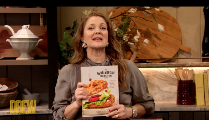 drew barrymore holds up a copy of the herbivorous butcher cookbook