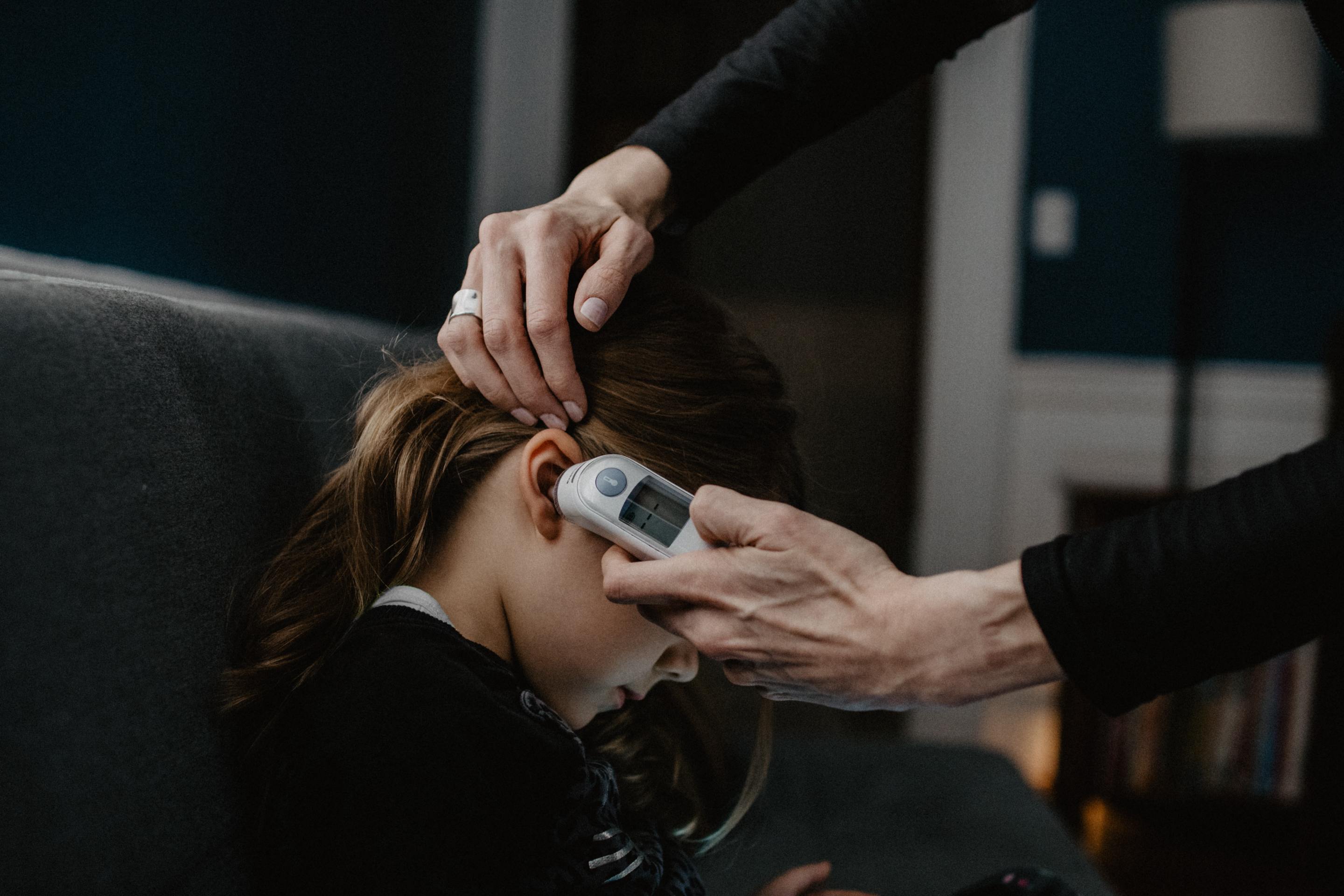 an adult takes a child's temperature with an ear thermometer