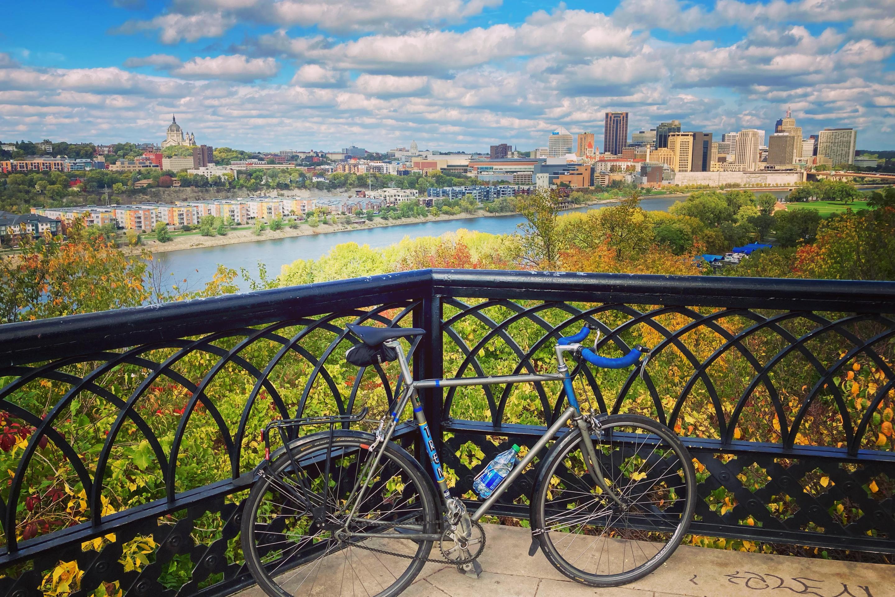 a bike leans up against a black grate overlooking the mississippi river, with the city in the background