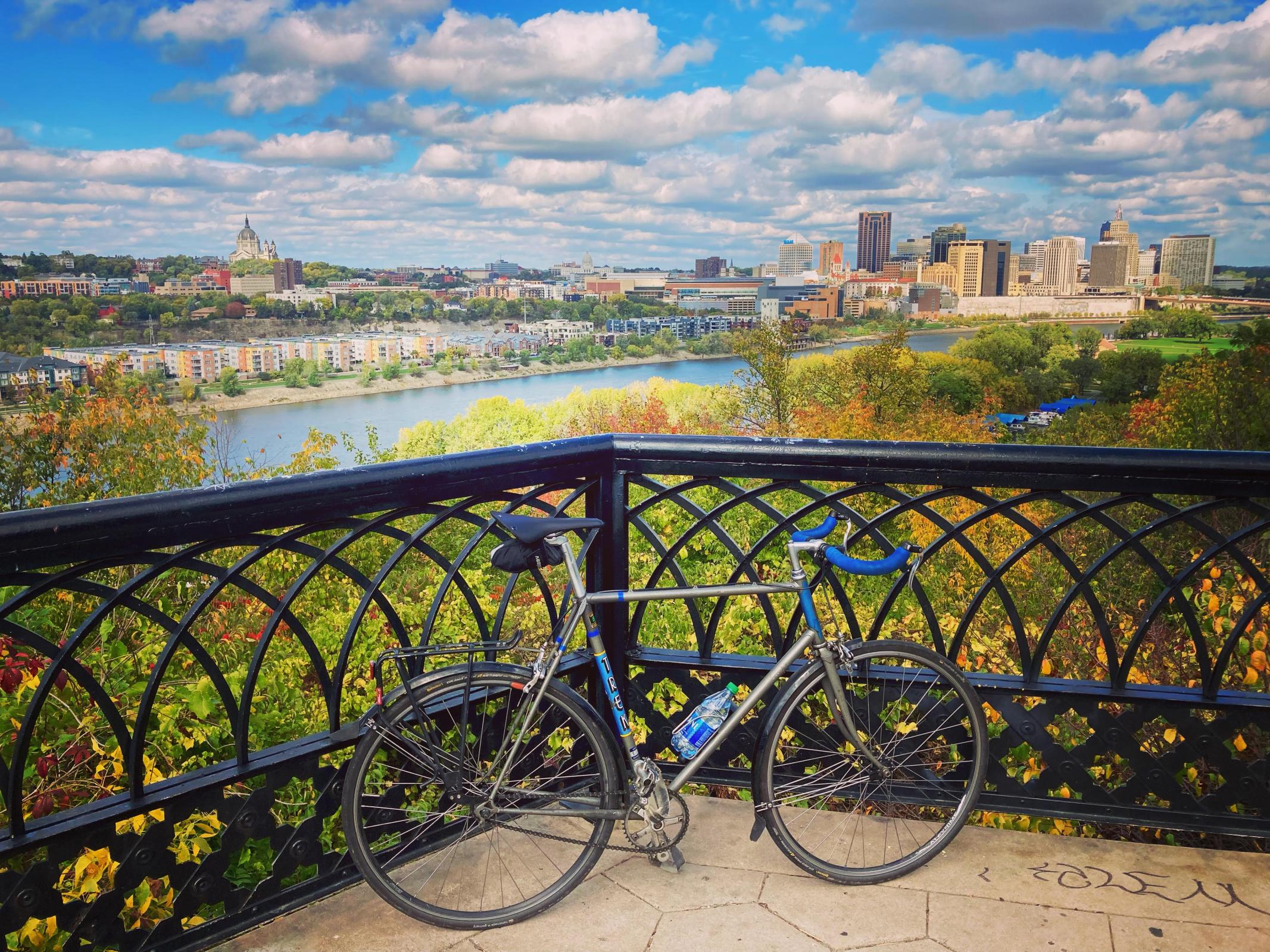a bike leans up against a black grate overlooking the mississippi river, with the city in the background