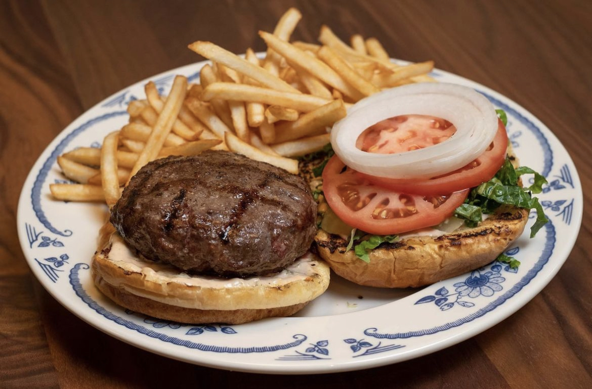 a burger that looks just... devine, portrayed open face with grill marks on its side and a pop of lettuce and tomato and onion