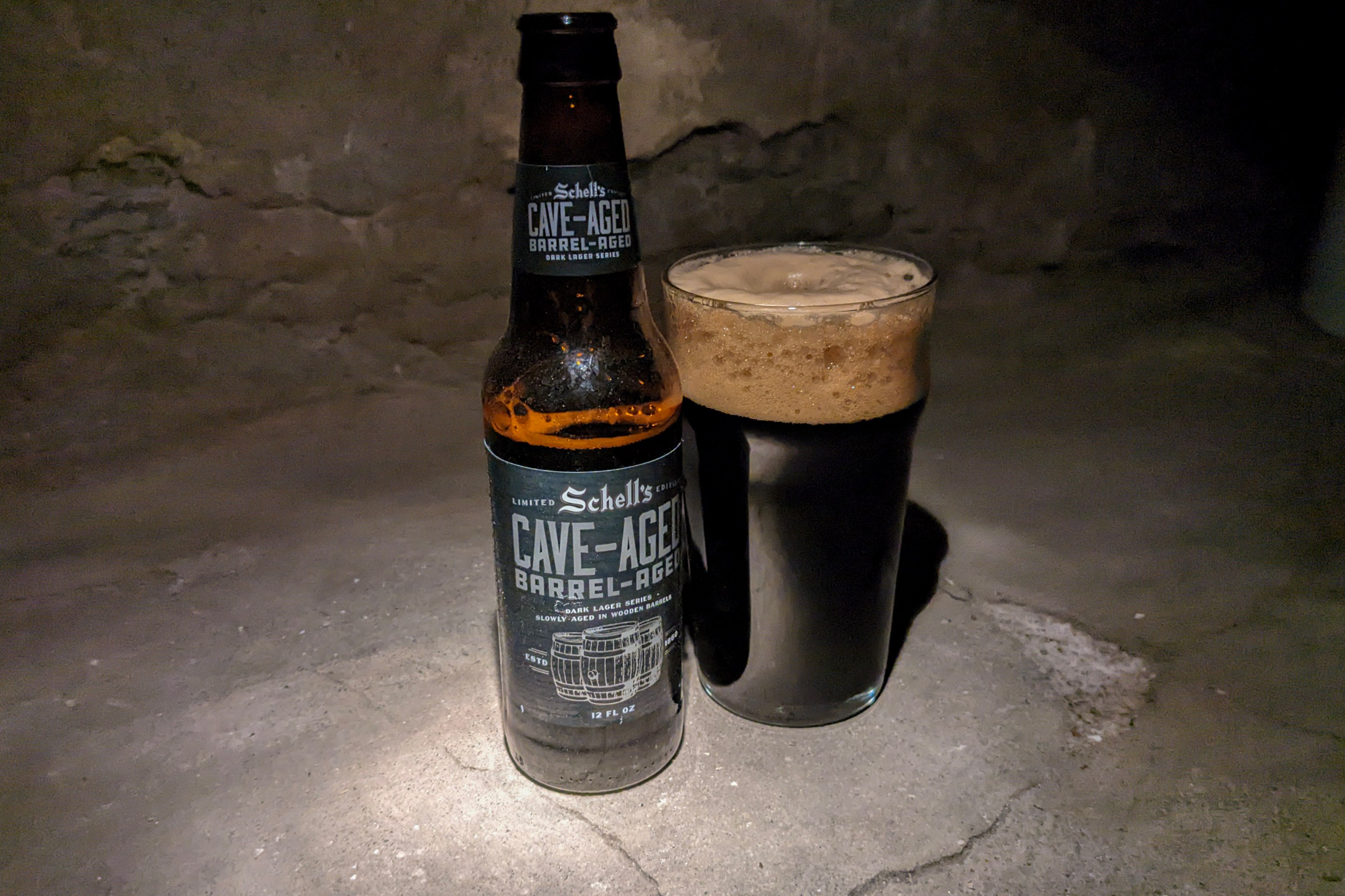 A dark, dark beer in a bottle sits next to a glass of it poured out. They're posed in a cave somewhere (or it could be a south Minneapolis basement)