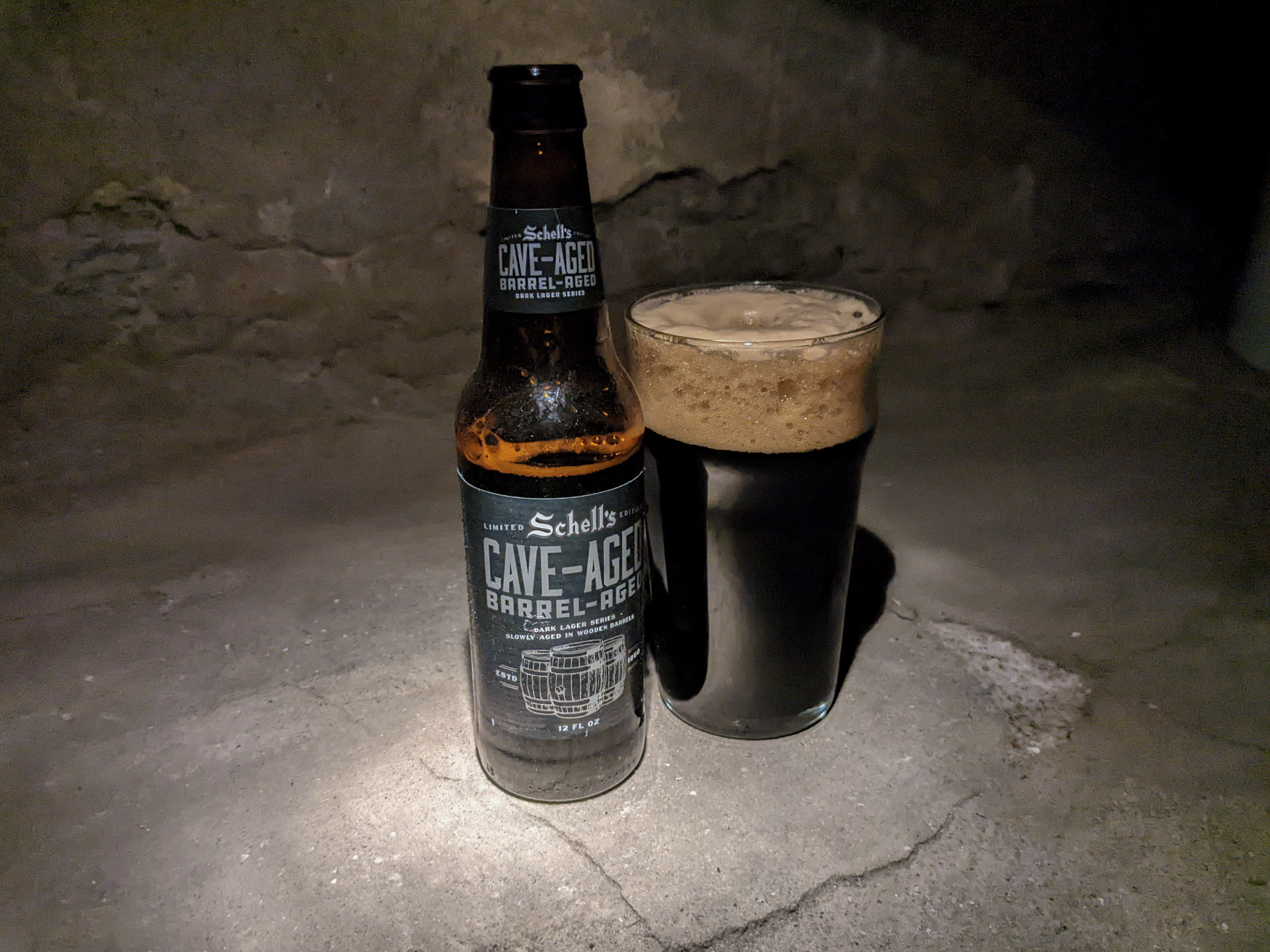 A dark, dark beer in a bottle sits next to a glass of it poured out. They're posed in a cave somewhere (or it could be a south Minneapolis basement)