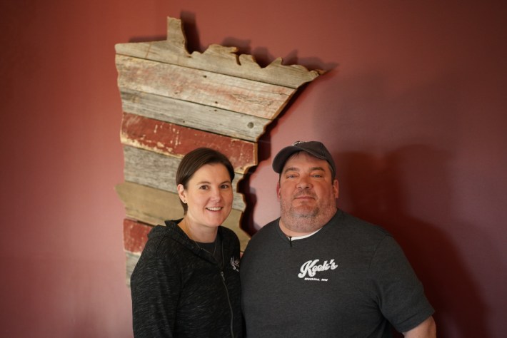a man and woman stand in front of a wooden cutout of minnesota