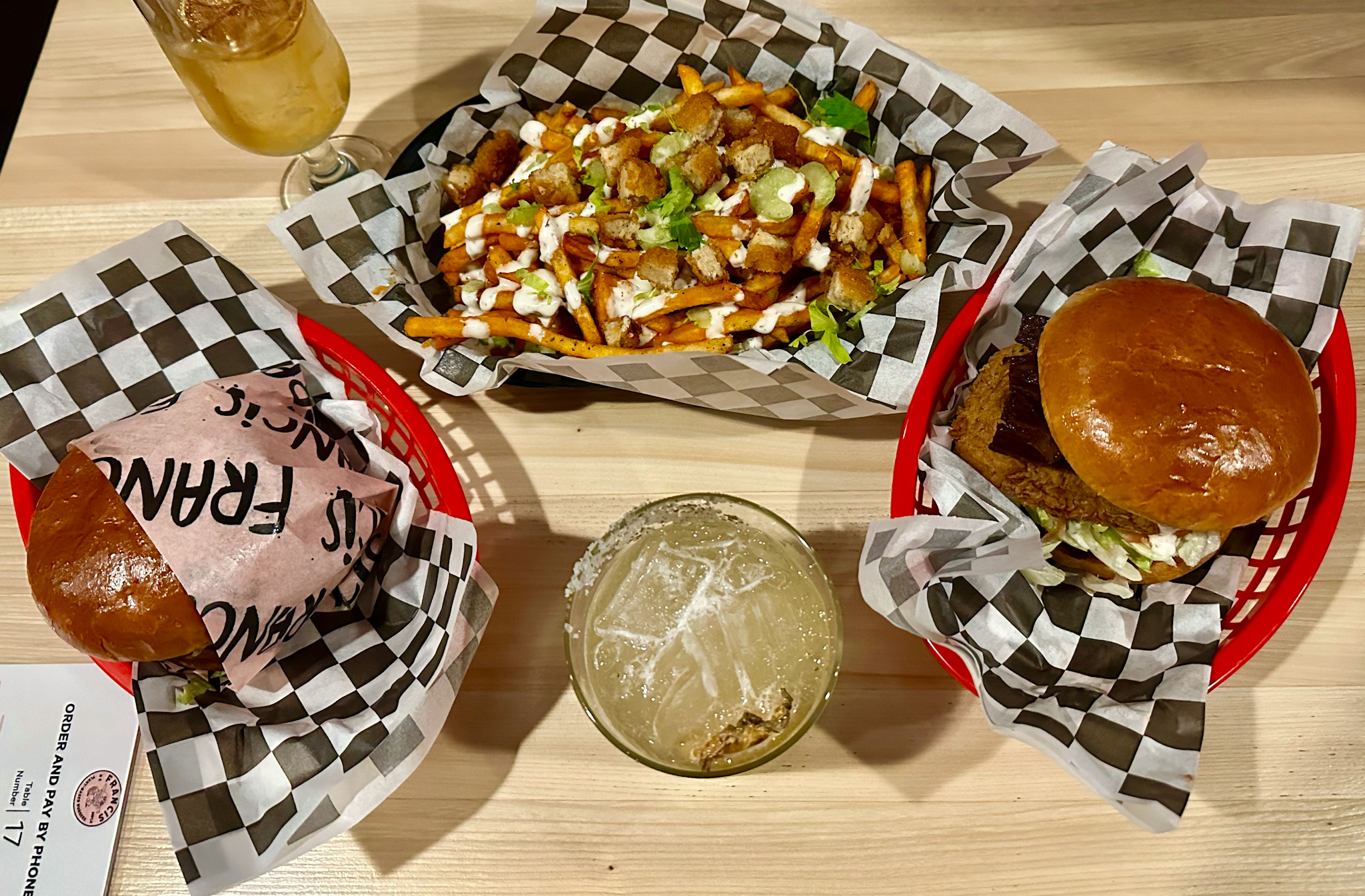 An overhead shot of two Francis sandwiches, a plate of buffalo fries, and two cocktails