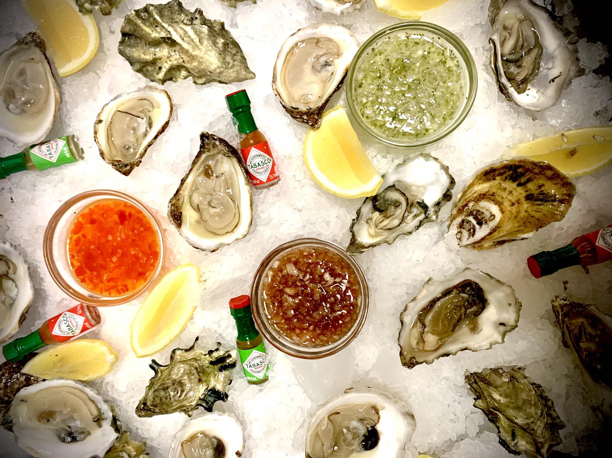 An overhead shot of oysters and assorted hot sauces on a bed of ice