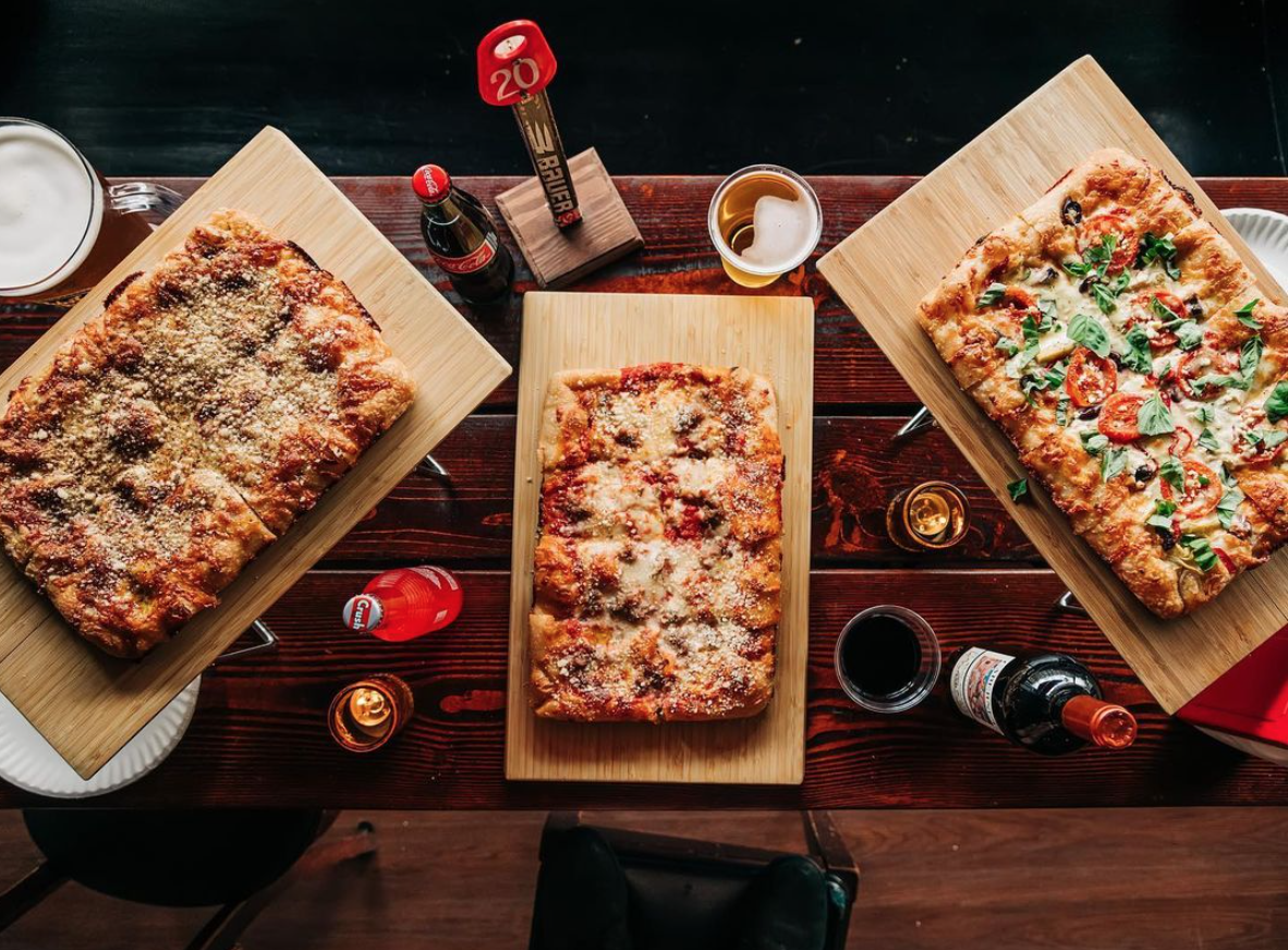 An overhead shot of three mario's pizzas, some wine, and a few coke bottles