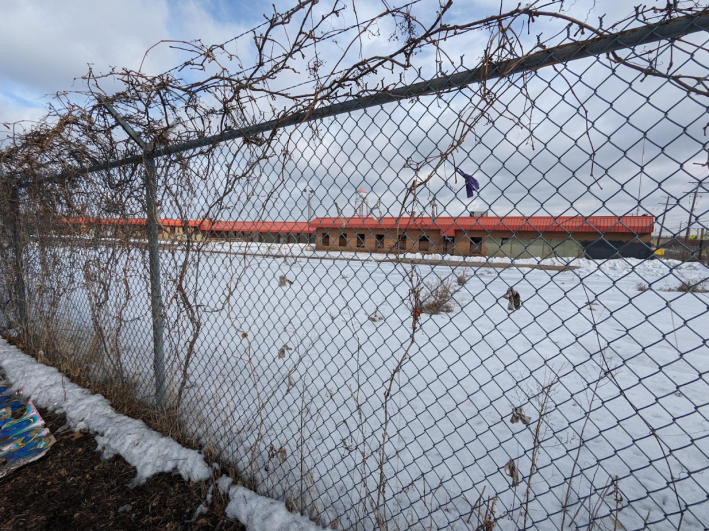 The Roof Depot site, obscured by a chain link fence topped with barbed wire.