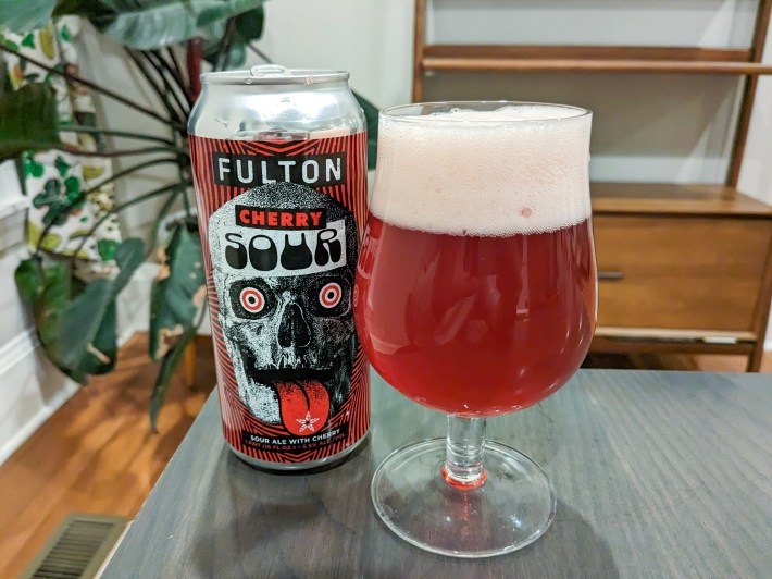 a glass of reddish beer next to a beer can with a skull on it