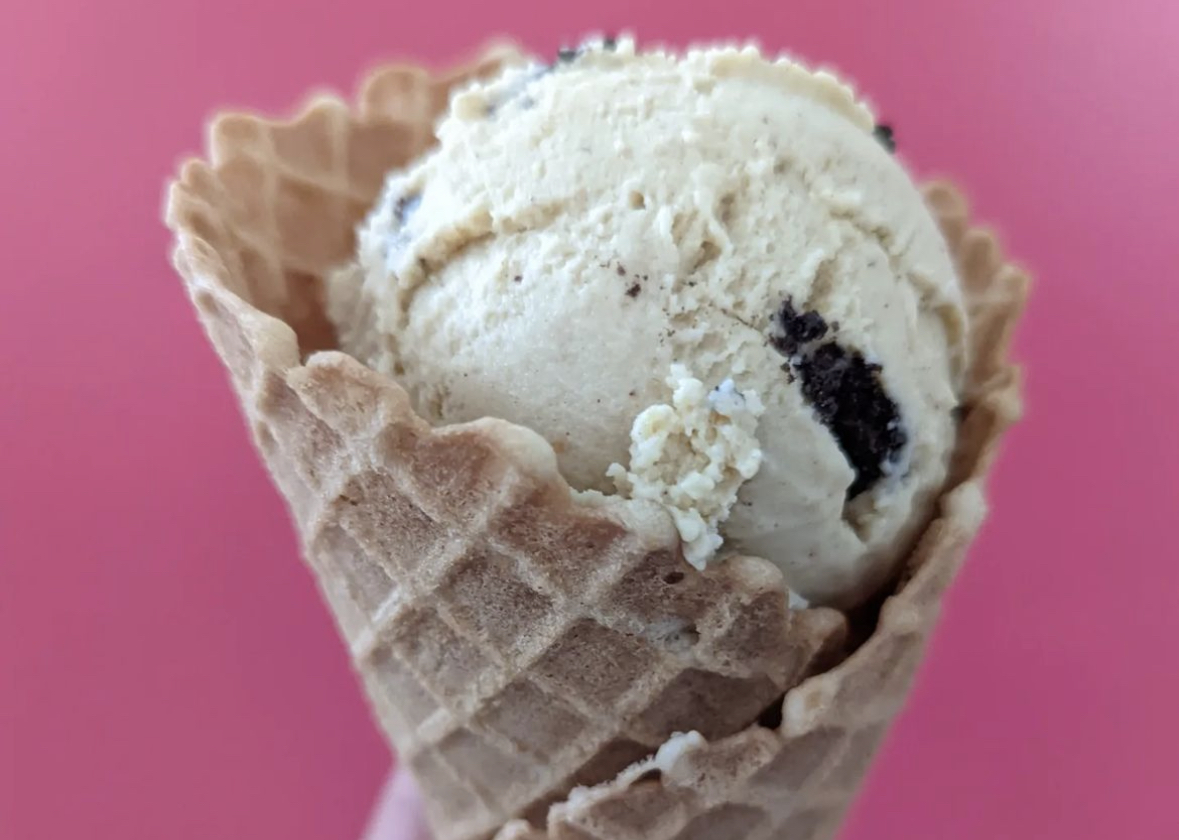 a scoop of vegan ice cream in a waffle cone on a bright pink background
