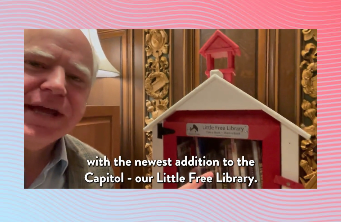 A screenshot of Governor Tim Walz speaking in front of a bright red little free library