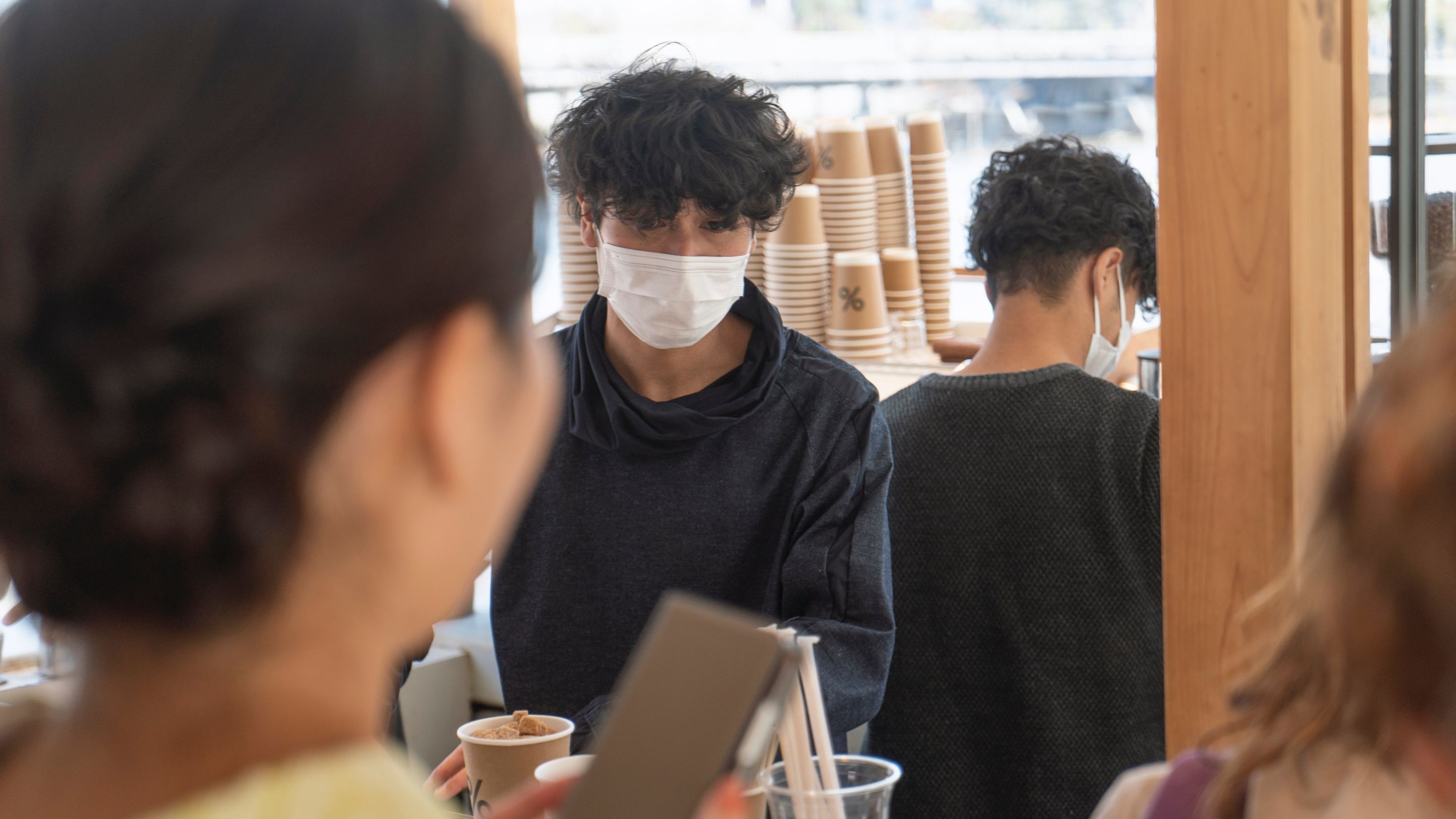 a person wearing a surgical mask serves coffee behind a counter