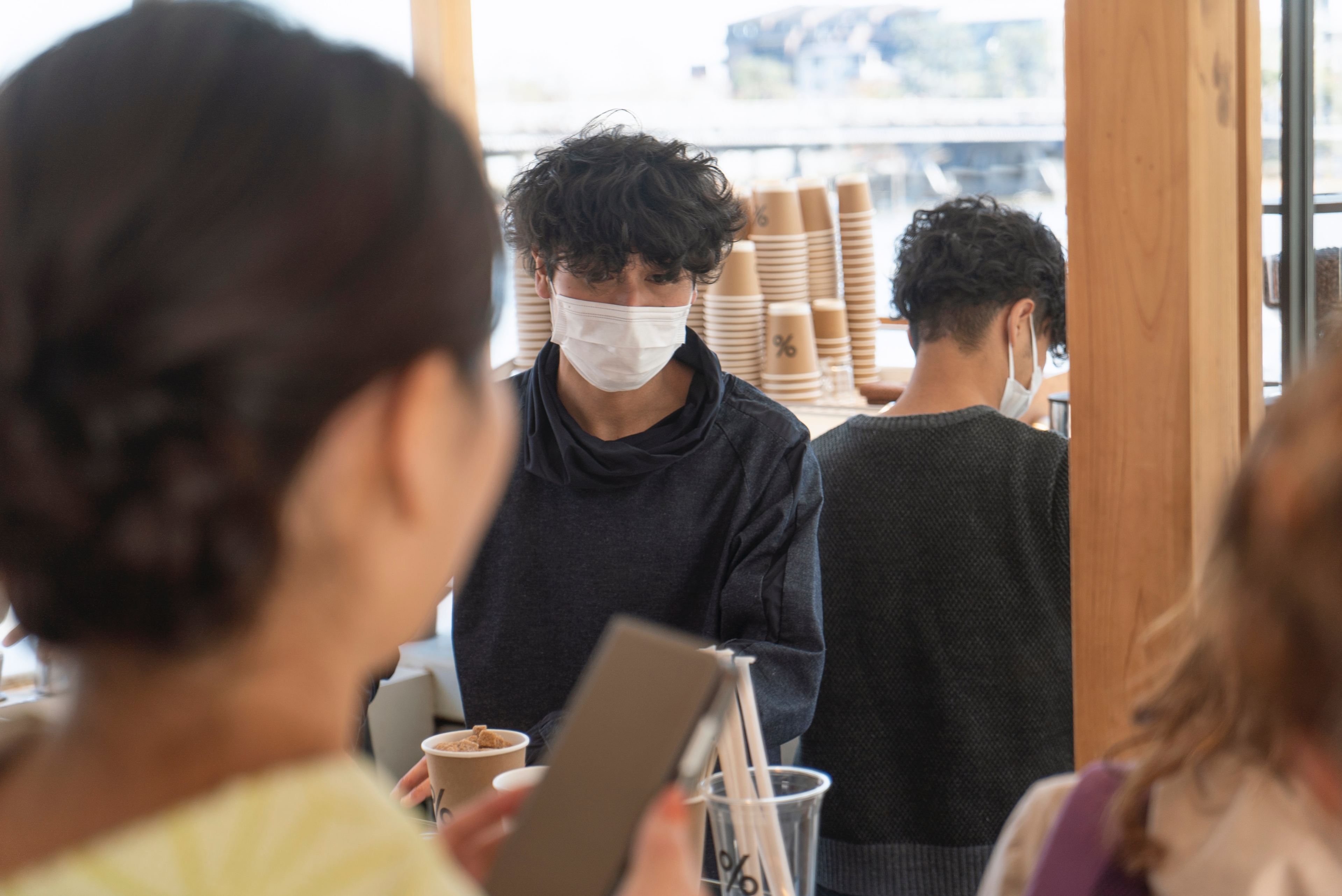 a person wearing a surgical mask serves coffee behind a counter