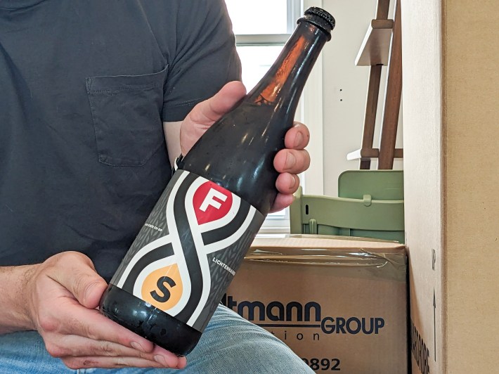 A pair of hands hold a big bottle of Lichtenhainer, posed in front of some packing boxes