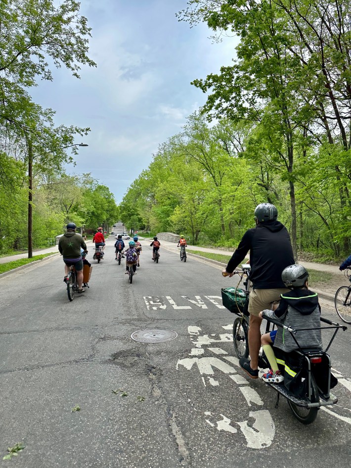 photographed from behind, a group of cyclists rides on a roadway in south minneapolis. one is crossing over a painted "bike blvd" message