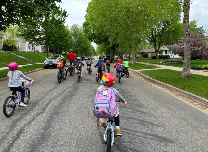 photographed from behind, a group of about eight kids on bikes with one adult takes over a minneapolis roadway