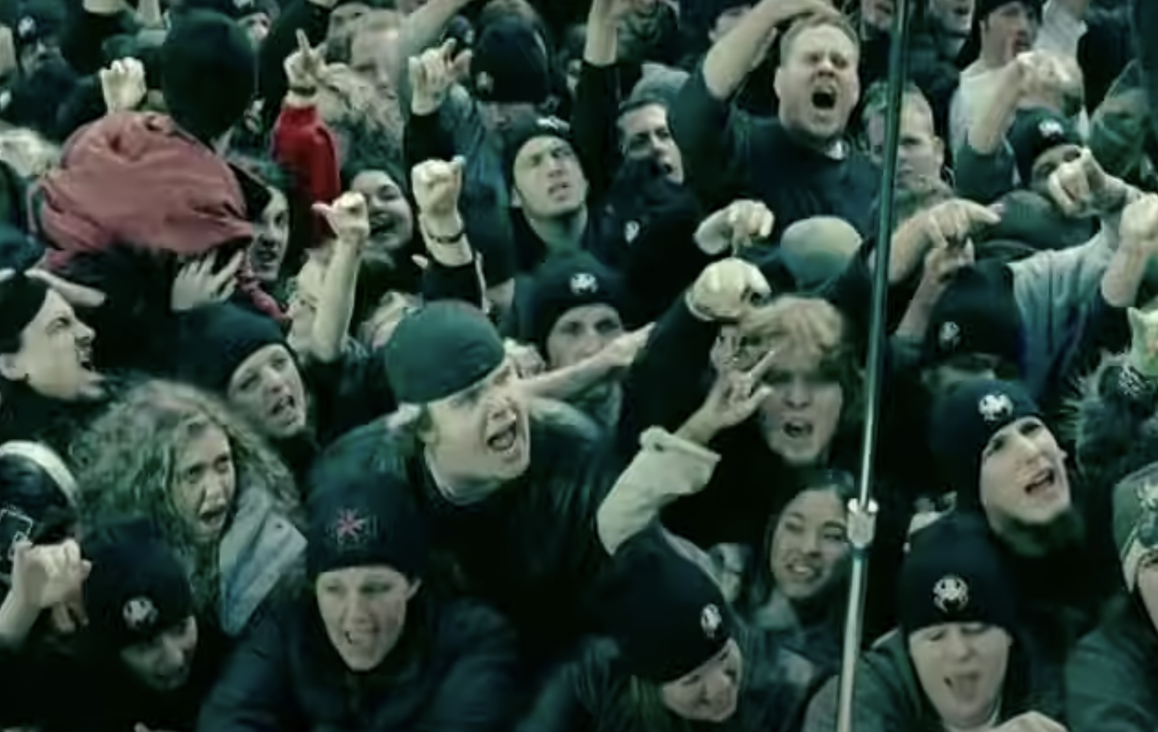 A crowd of screaming white teens throwing up devil horns.